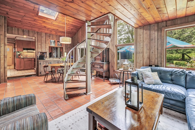 living room with lofted ceiling, stairs, wooden walls, light tile patterned floors, and a skylight