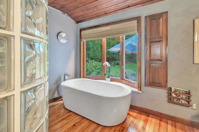 bathroom with baseboards, hardwood / wood-style floors, wooden ceiling, and a soaking tub