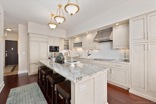 kitchen featuring wall chimney exhaust hood, black appliances, tasteful backsplash, a breakfast bar, and dark wood-type flooring