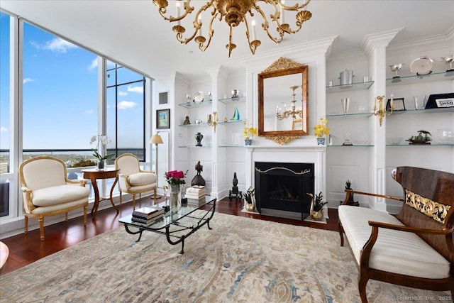 living room featuring wood finished floors, ornamental molding, built in features, a chandelier, and a wall of windows