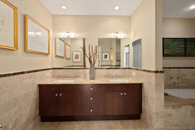 bathroom with tile walls, a wainscoted wall, double vanity, and a tub to relax in