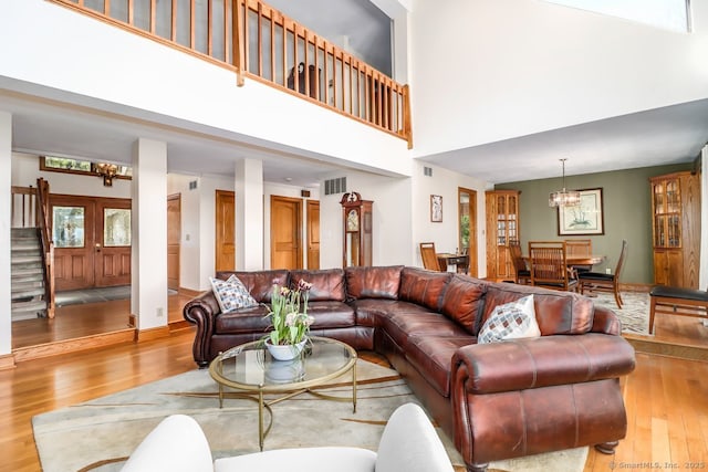 living room featuring an inviting chandelier, visible vents, stairs, wood finished floors, and a high ceiling