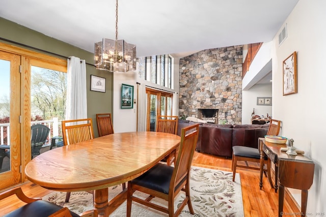dining room featuring a fireplace, light wood finished floors, a notable chandelier, and visible vents