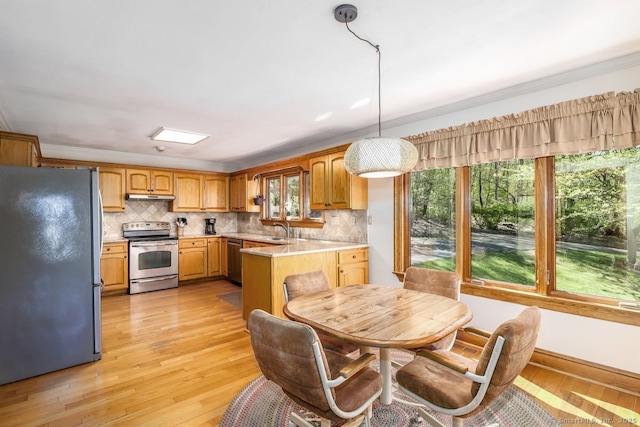 kitchen with stainless steel appliances, a sink, backsplash, light countertops, and light wood-type flooring