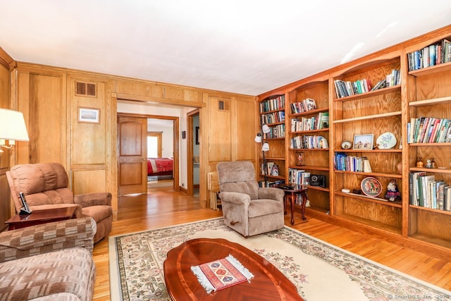 living area with wooden walls, light wood-style flooring, and visible vents