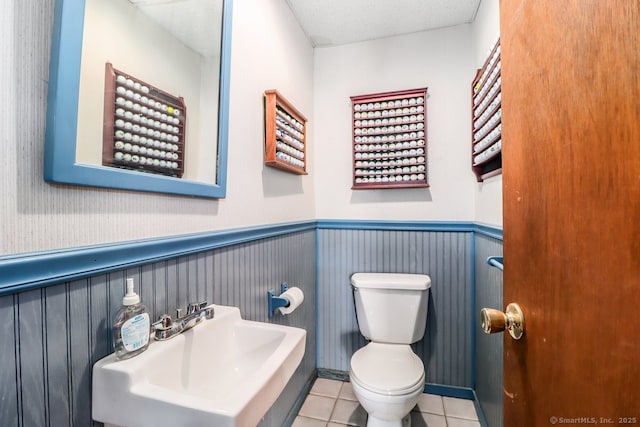 half bath featuring tile patterned floors, a wainscoted wall, toilet, and a sink