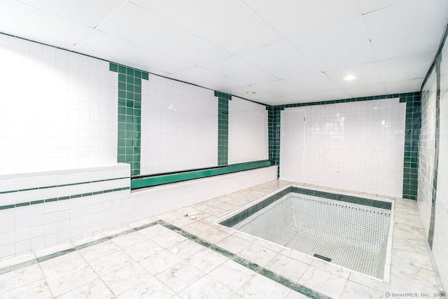 interior space with a paneled ceiling and tile walls