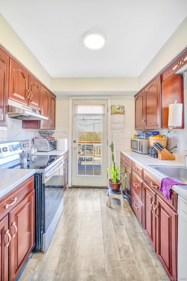kitchen with stainless steel appliances, under cabinet range hood, light countertops, and light wood-type flooring