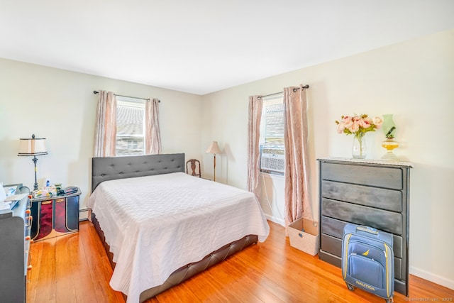 bedroom featuring multiple windows, light wood finished floors, baseboards, and baseboard heating