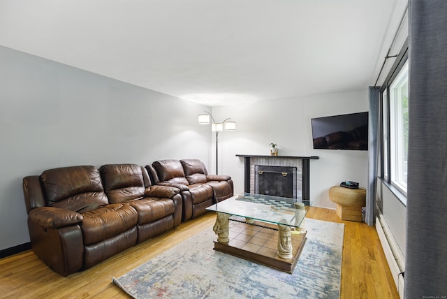 living room with healthy amount of natural light, a baseboard radiator, light wood finished floors, and a fireplace