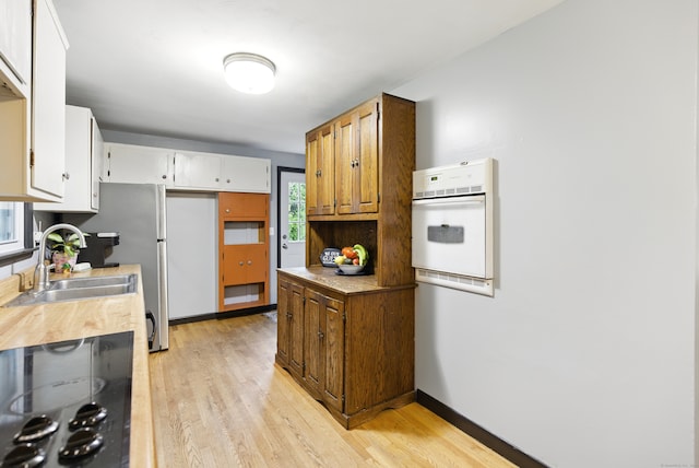 kitchen featuring oven, light wood finished floors, a sink, light countertops, and baseboards