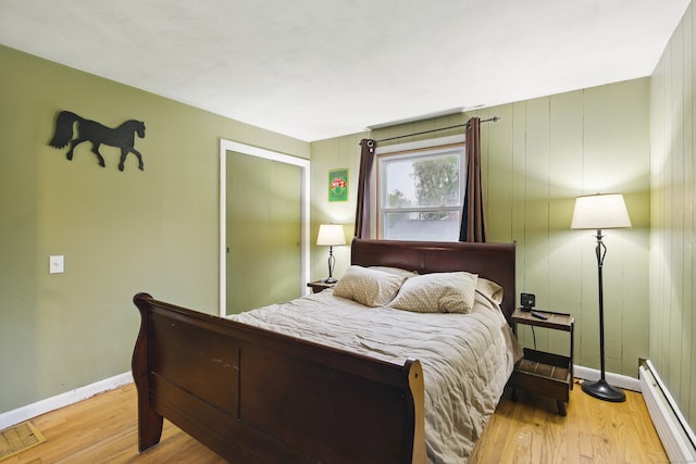 bedroom featuring a baseboard radiator, baseboards, and light wood-style flooring