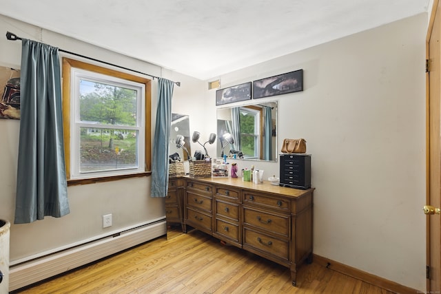 bedroom with baseboard heating, light wood finished floors, and baseboards