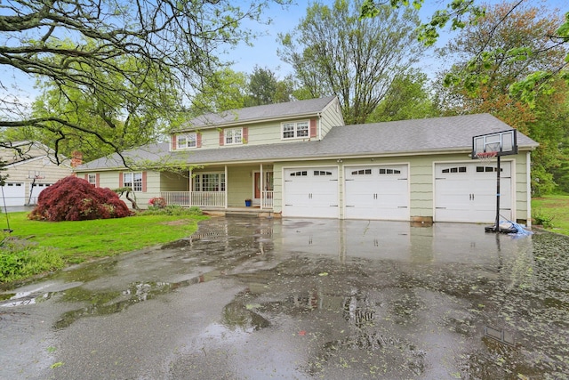 traditional-style home with a porch, a front lawn, an attached garage, and driveway