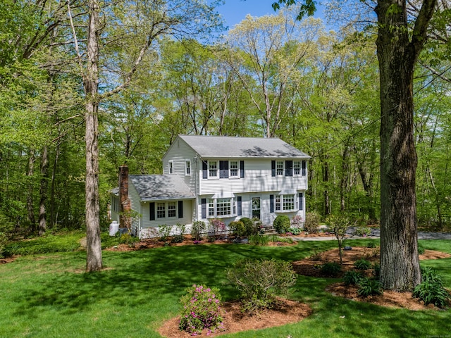 colonial house featuring a chimney, a front yard, and a shingled roof