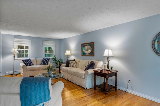 living room with a textured ceiling, light wood-type flooring, baseboards, and a baseboard heating unit