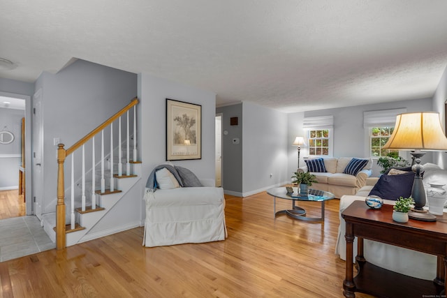 living room with light wood finished floors, stairway, a textured ceiling, and baseboards