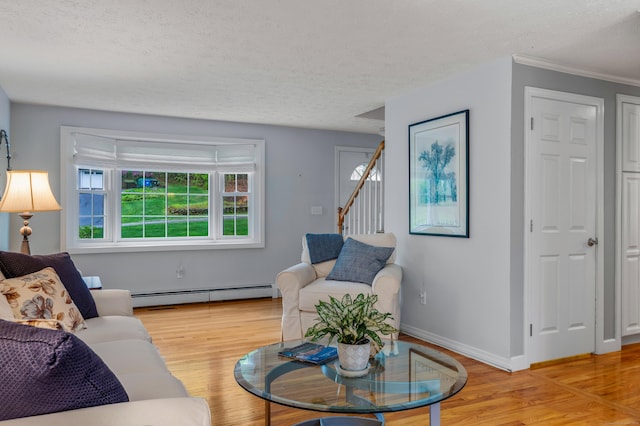 living room featuring a baseboard heating unit, a textured ceiling, light wood-type flooring, baseboards, and crown molding