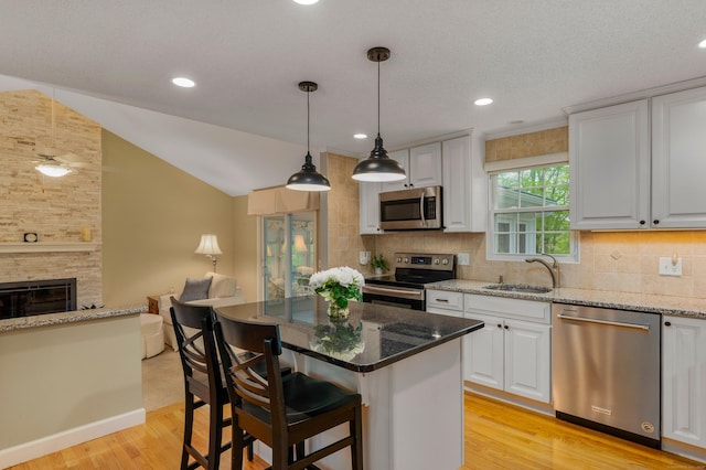 kitchen featuring stainless steel appliances, light wood-style floors, open floor plan, tasteful backsplash, and light stone countertops