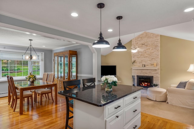 kitchen featuring light wood finished floors, open floor plan, white cabinets, a stone fireplace, and a kitchen island