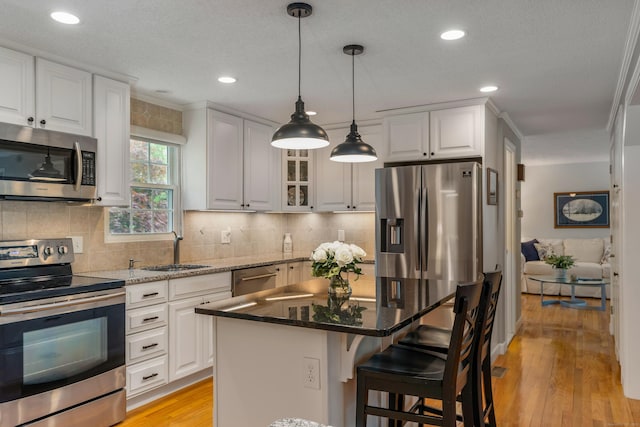 kitchen with stainless steel appliances, a sink, white cabinetry, a breakfast bar area, and light wood-style floors