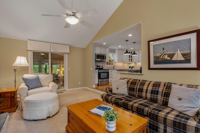 living area featuring light carpet, ceiling fan, healthy amount of natural light, high vaulted ceiling, and baseboards