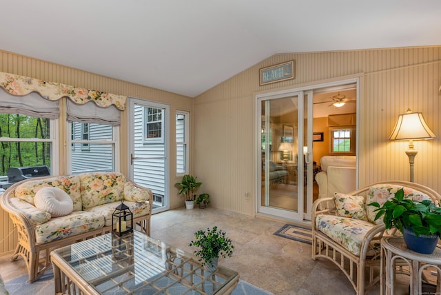 living room featuring vaulted ceiling, wooden walls, and ceiling fan