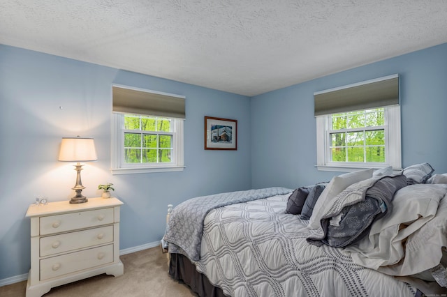 bedroom with multiple windows, light carpet, baseboards, and a textured ceiling