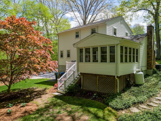 rear view of property featuring a chimney, a sunroom, stairs, and a yard