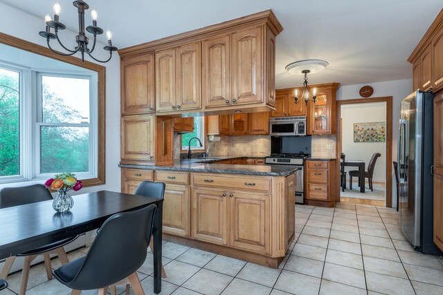 kitchen with a chandelier, stainless steel appliances, a sink, decorative backsplash, and brown cabinets
