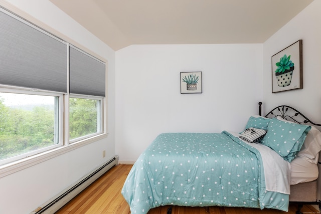 bedroom featuring a baseboard radiator, lofted ceiling, wood finished floors, and baseboards