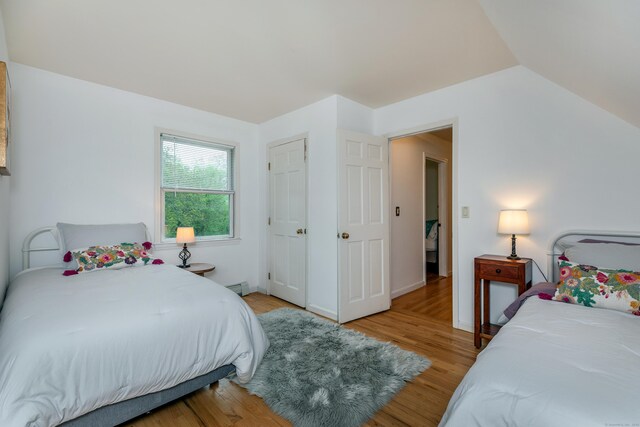 bedroom featuring light wood-style floors, baseboard heating, and lofted ceiling
