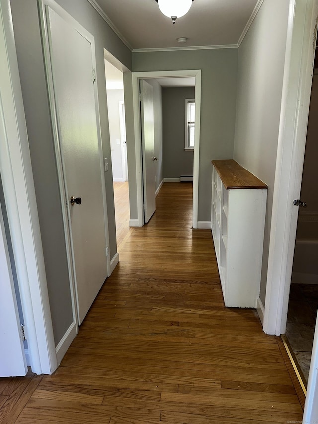corridor featuring crown molding, baseboards, wood finished floors, and a baseboard heating unit