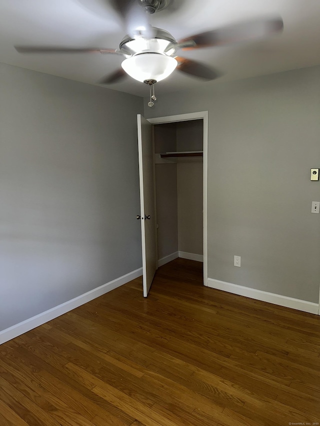 unfurnished bedroom featuring dark wood-style floors, a closet, baseboards, and ceiling fan