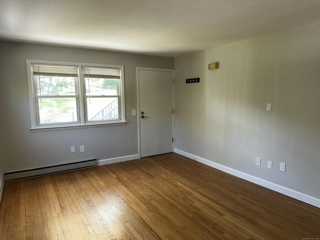 unfurnished room featuring wood-type flooring, baseboards, and a baseboard radiator