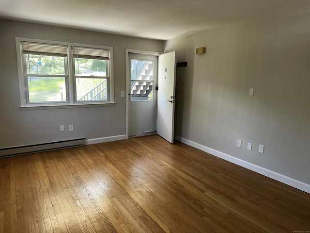 unfurnished room featuring hardwood / wood-style flooring, a baseboard heating unit, and baseboards