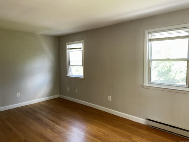 unfurnished room with a baseboard heating unit, wood finished floors, and baseboards