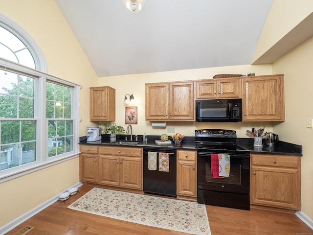 kitchen featuring black appliances, a sink, dark countertops, light wood-style floors, and baseboards