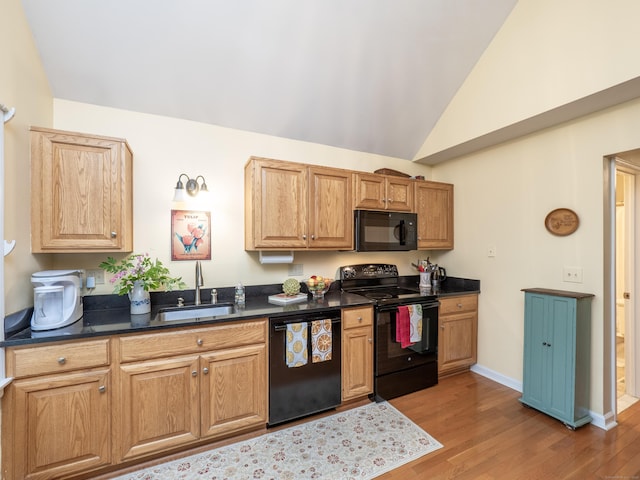 kitchen with black appliances, a sink, dark countertops, light wood-style flooring, and vaulted ceiling