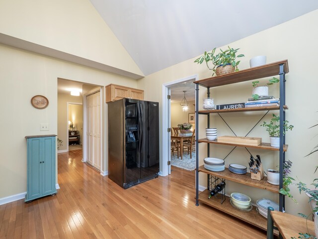 kitchen featuring light wood-style flooring, vaulted ceiling, baseboards, black refrigerator with ice dispenser, and blue cabinets