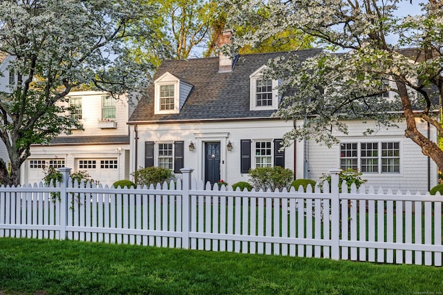 new england style home with an attached garage, roof with shingles, a fenced front yard, and a chimney