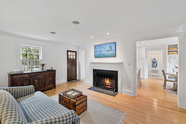 living area with radiator heating unit, crown molding, a fireplace with flush hearth, light wood finished floors, and recessed lighting