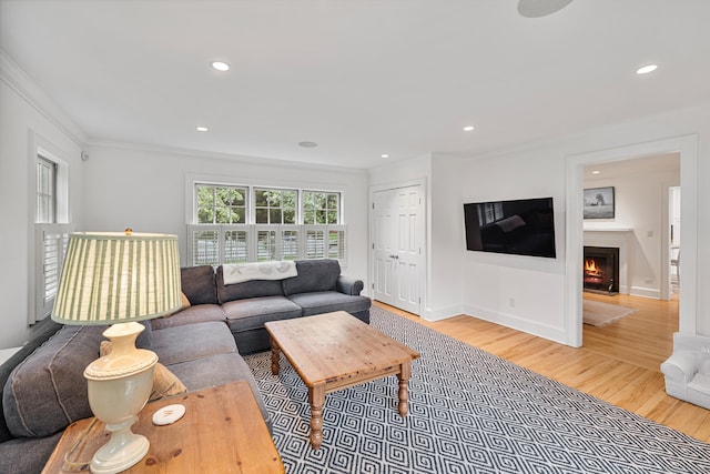 living room with crown molding, wood finished floors, a fireplace with flush hearth, and recessed lighting