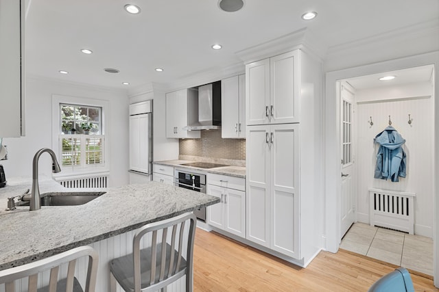 kitchen with a sink, wall chimney exhaust hood, stainless steel oven, white cabinetry, and black electric cooktop