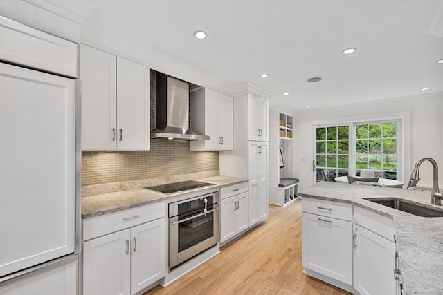 kitchen featuring wall chimney exhaust hood, stainless steel oven, a sink, paneled built in refrigerator, and black electric cooktop