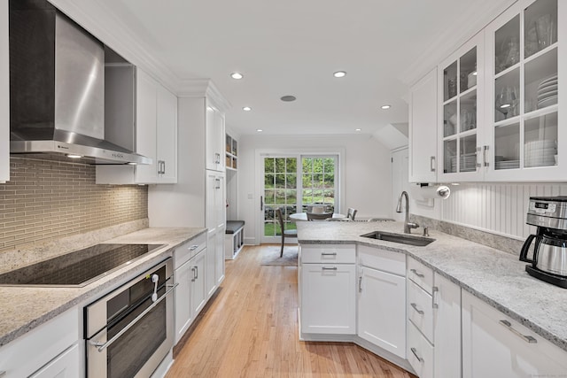 kitchen with wall chimney range hood, stainless steel oven, a sink, black electric stovetop, and white cabinetry