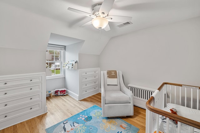 bedroom with light wood-style flooring, vaulted ceiling, a crib, ceiling fan, and baseboards
