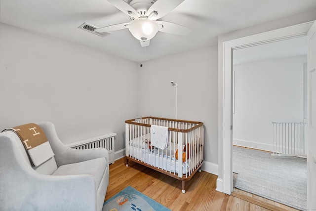 bedroom with wood finished floors, baseboards, a crib, and ceiling fan