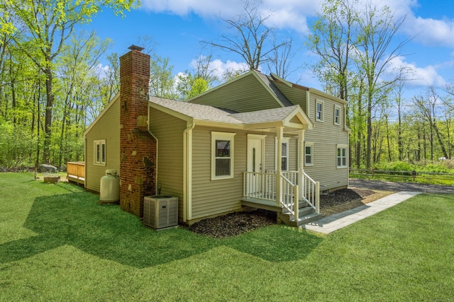rear view of house with a chimney, a shingled roof, and central AC unit