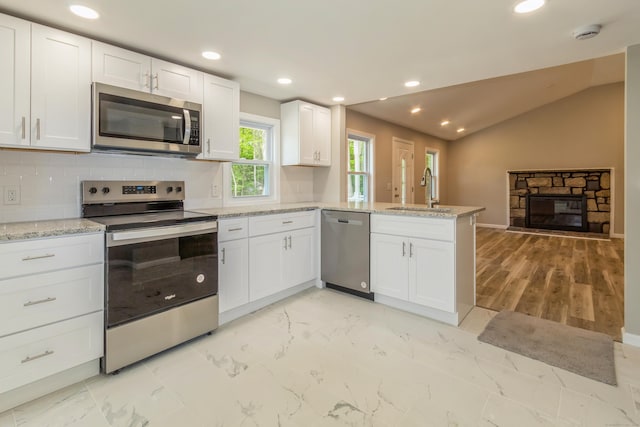 kitchen with stainless steel appliances, a sink, a peninsula, white cabinetry, and decorative backsplash